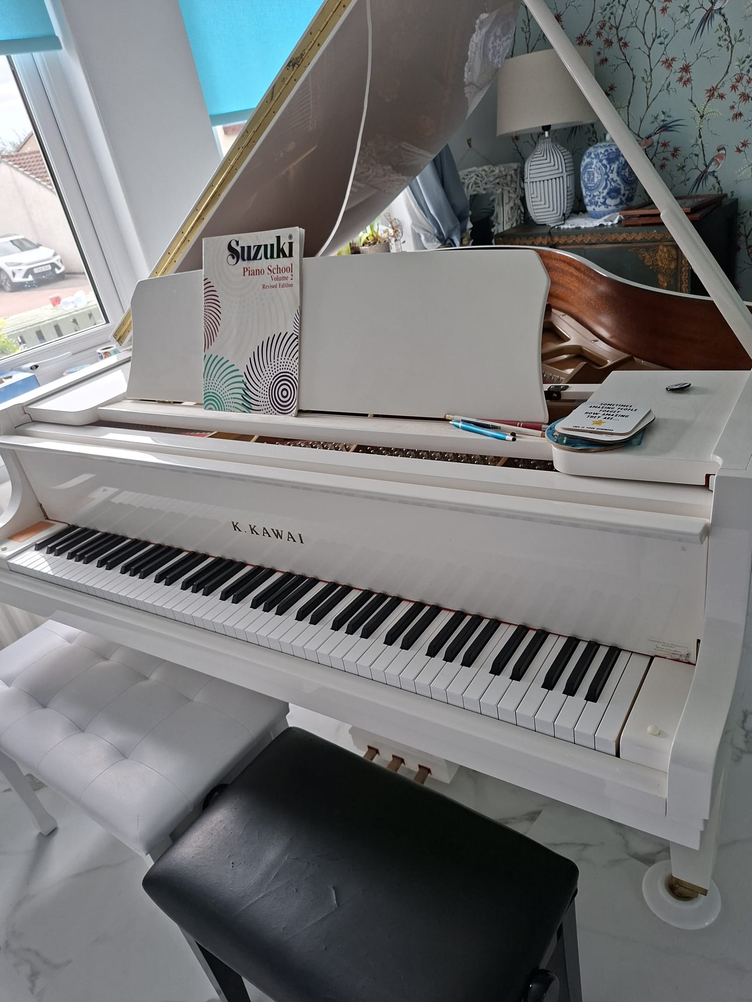 White Kawai grand piano with a Suzuki piano book on its music stand